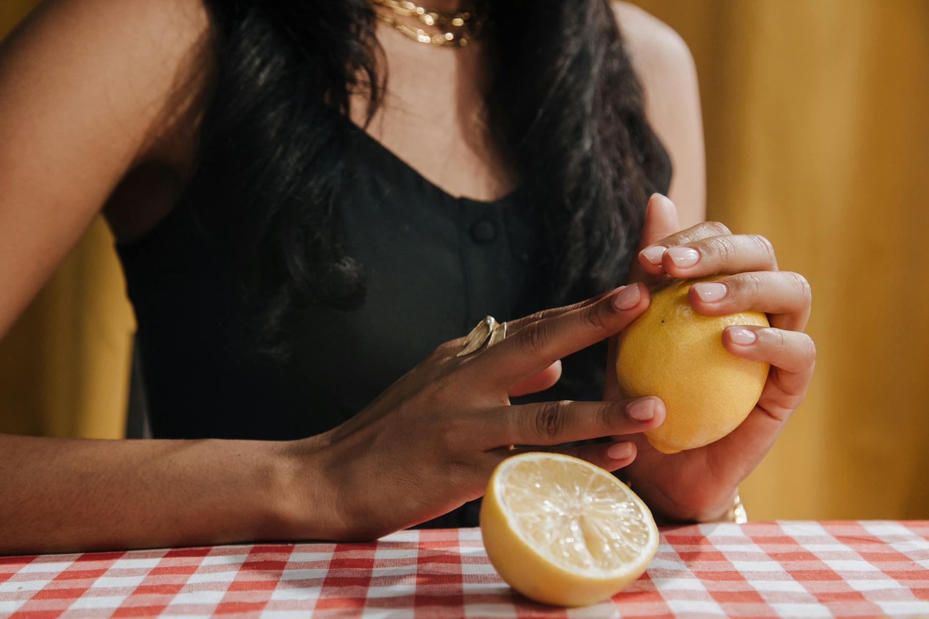 A close-up of a woman with black hair holding a fresh lemon at a dining table.