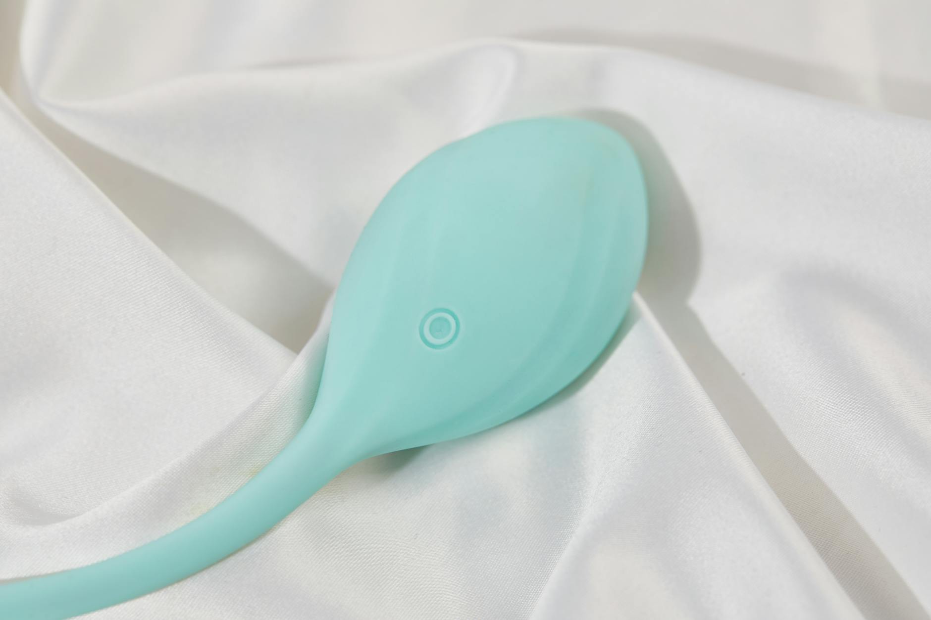 A sleek teal clitoral vibrator on smooth white silk, showcasing design and texture