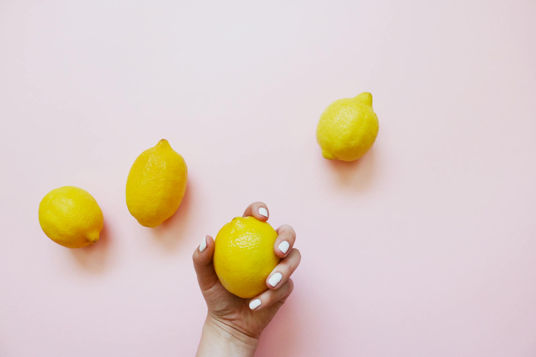 A hand holding a fresh lemon on a soft pink background, symbolizing the delicate nature of hormonal sensitivity shifts