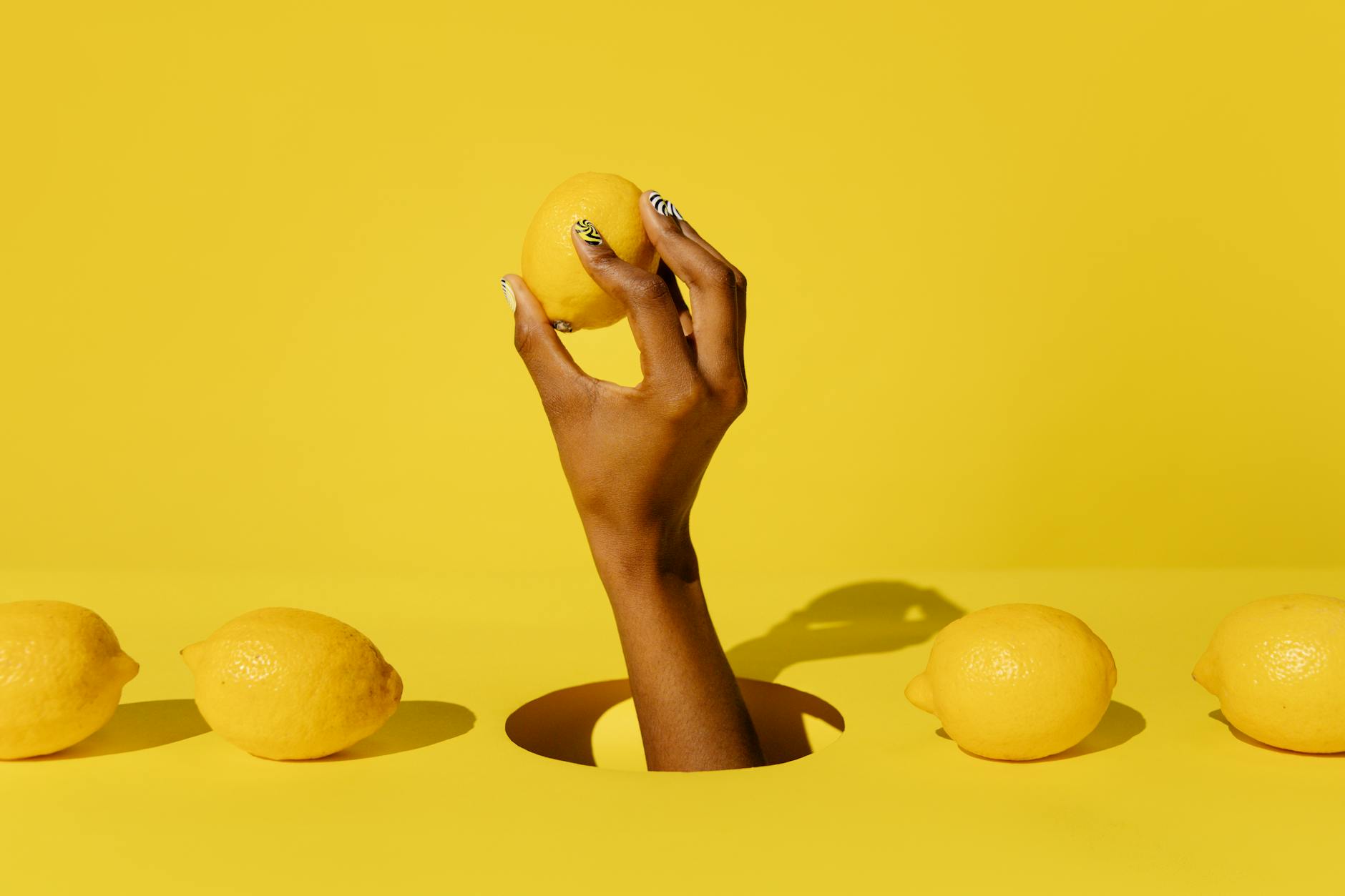 Hand holding a fresh lemon against a vivid yellow background, symbolizing the citrusy design of clitoral vibrators