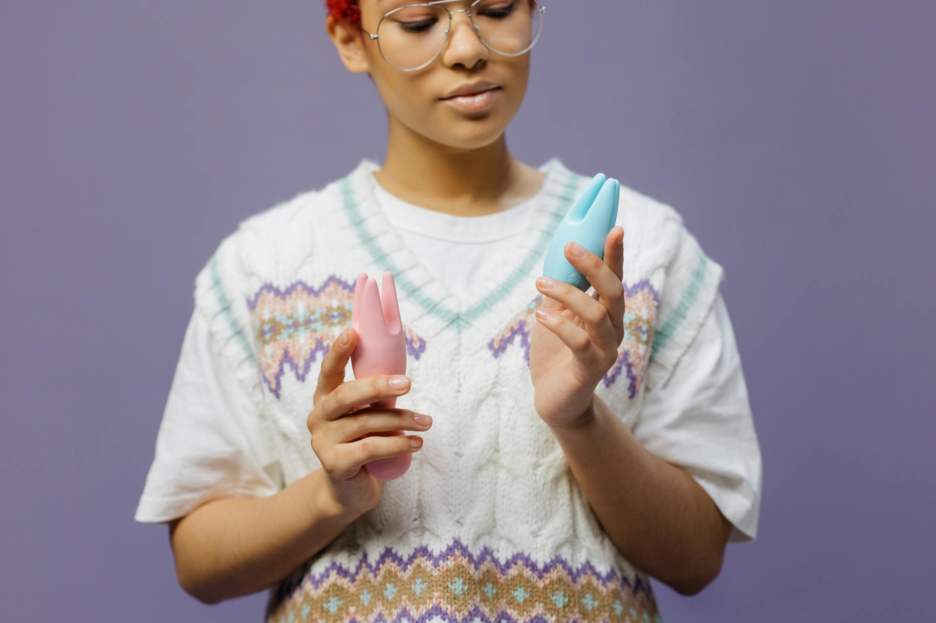 Person holding lemon-colored and pink clitoral vibrators thoughtfully