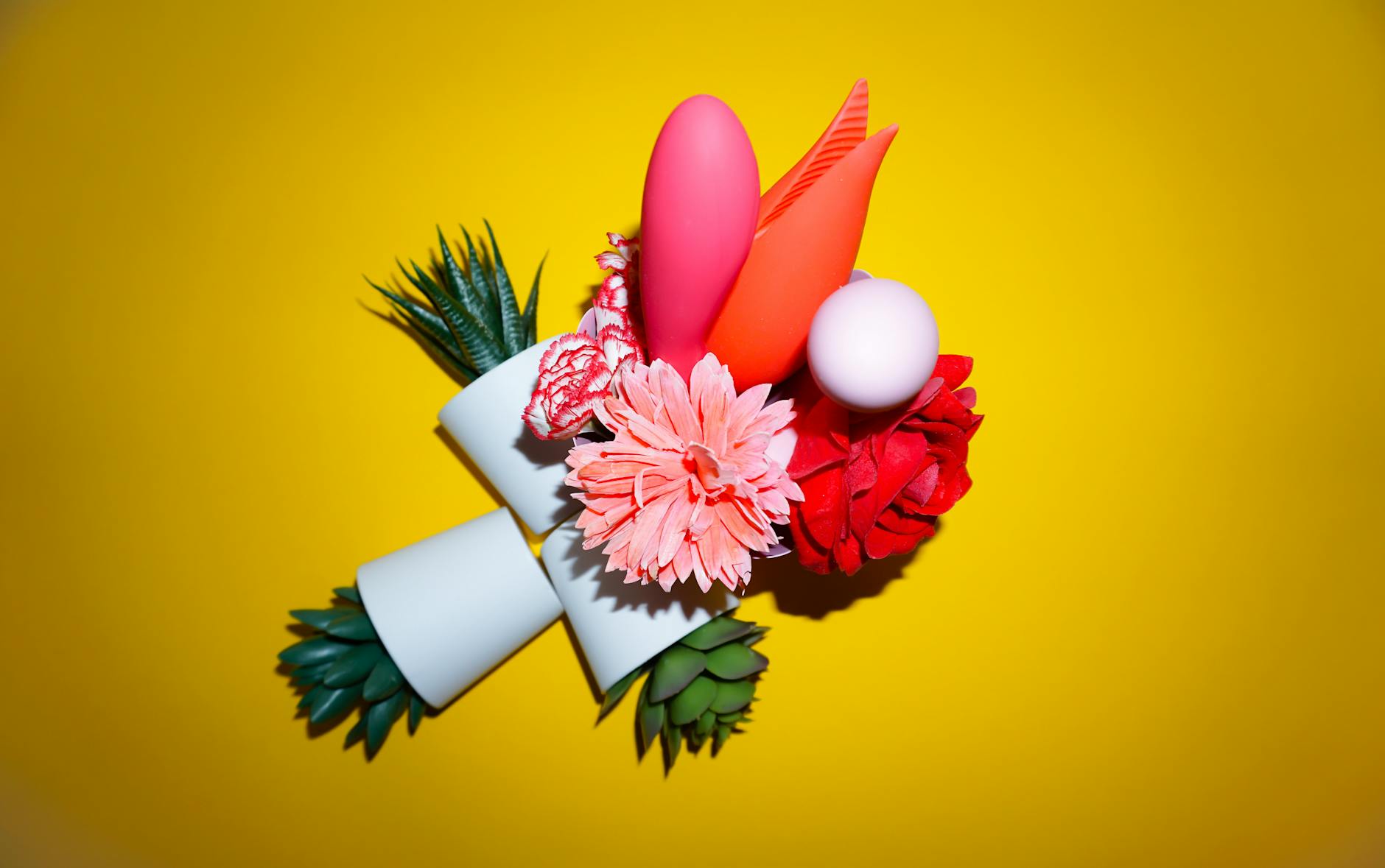 Array of vibrators and adult toys arranged on a bright yellow surface