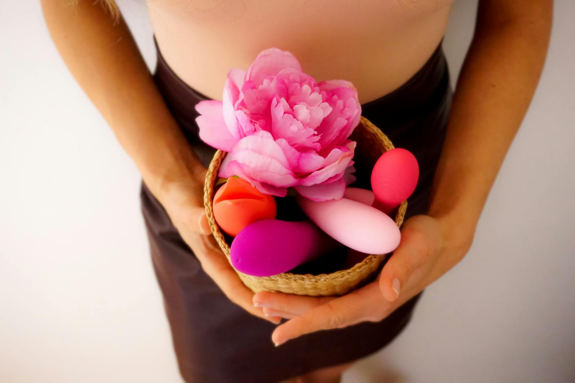 A basket holding colorful vibrators and a pink flower, representing intimate wellness tools